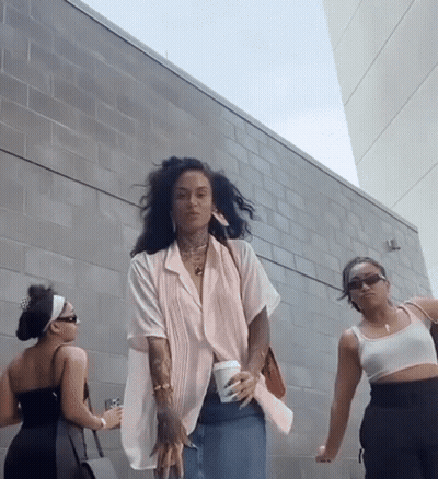 Three Women Are Standing In Front Of A Brick Wall And One Is Holding A Cup Of Coffee GIF