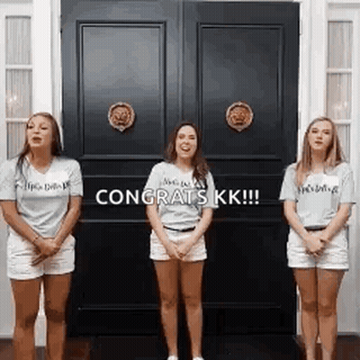 Three Women Are Standing In Front Of A Door With The Words `` Congrats Kk '' Written On It . GIF