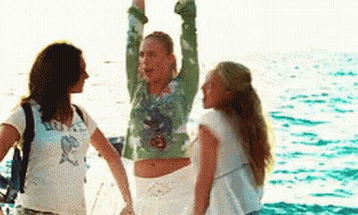 Three Women Are Standing On A Boat In The Ocean . One Of The Women Is Raising Her Arms In The Air . GIF