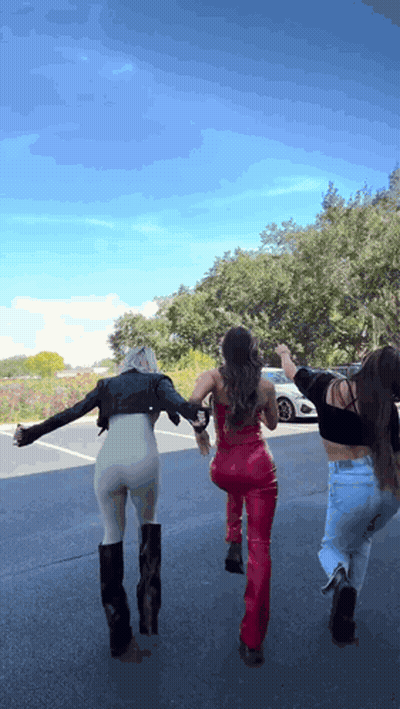 Three Women Are Walking Down A Street With Their Arms Outstretched . GIF