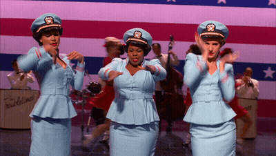 Three Women In Blue Uniforms Dancing In Front Of Band GIF