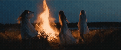 Three Women In White Robes Are Standing Around A Fire At Night . GIF
