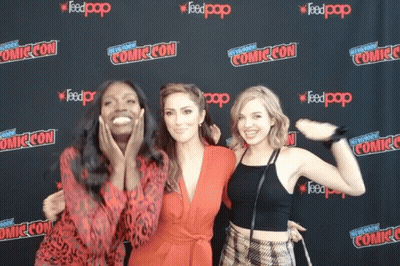 Three Women Pose In Front Of A Wall That Says Comic Con On It GIF