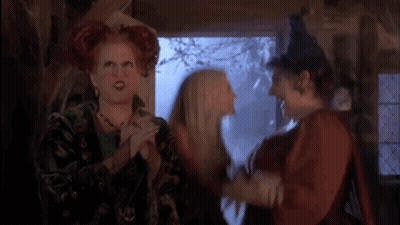 Three Women Standing With One In Witch Hat GIF
