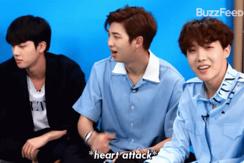 Three Young Men Are Sitting In Front Of A Blue Wall And One Of Them Is Saying " Heart Attack " GIF