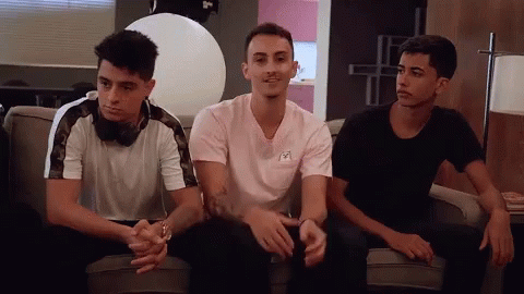 Three Young Men Are Sitting On A Couch With One Wearing A Pink Shirt GIF