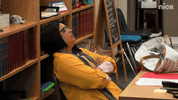 Tired Teacher Leaning On Bookshelf GIF