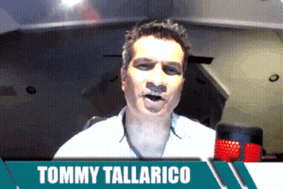 Tommy Tallarico Talking Into Microphone In Front Of Green Banner GIF