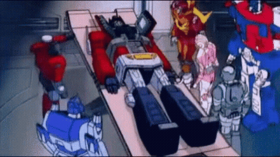 Transformers Standing Around Robot Laying On Bed GIF