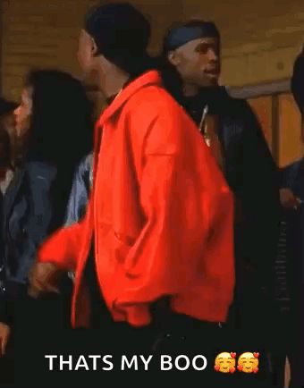 Tupac Shakur Is Wearing A Red Jacket And Smoking A Cigarette While Standing In Front Of A Group Of People . GIF