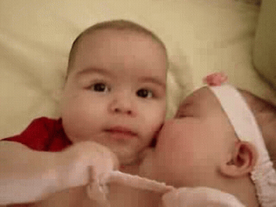Two Babies Are Kissing Each Other On The Cheeks . GIF