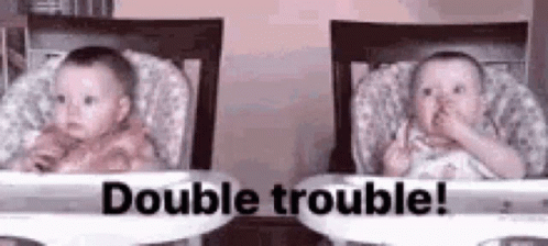 Two Babies Are Sitting In High Chairs And One Of Them Is Making A Funny Face . GIF