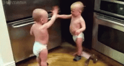 Two Babies In Diapers Are Standing Next To Each Other In A Kitchen And Giving Each Other A High Five . GIF