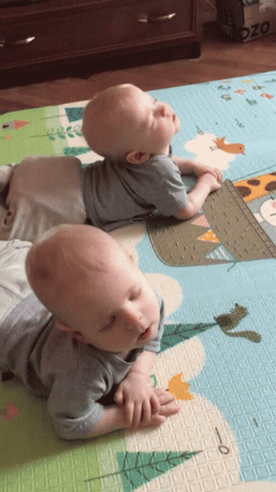 Two Babies Laying On A Mat With A Giraffe On It And A Box That Says Ozo On It GIF