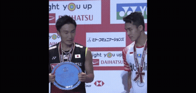 Two Badminton Players Holding A Trophy In Front Of A Sign That Says Light You Up GIF