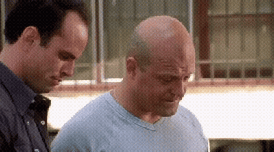 Two Bald Men Standing, One Looking Down GIF