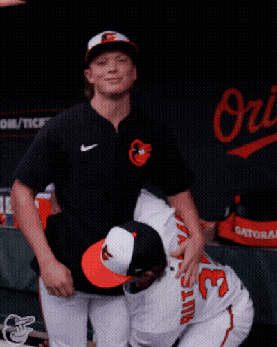 Two Baseball Players Are Hugging Each Other In Front Of A Sign That Says Orioles GIF