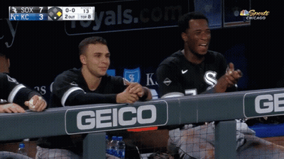 two baseball players are sitting in the dugout with a geico sign