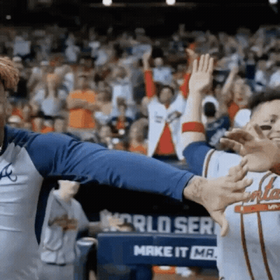 Two Baseball Players Giving Each Other A High Five In Front Of A Sign That Says World Series GIF