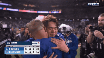 Two Baseball Players Hugging In Front Of Dodgers Scoreboard GIF