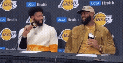 Two Basketball Players Are Sitting At A Table With A Lakers Logo In The Background GIF