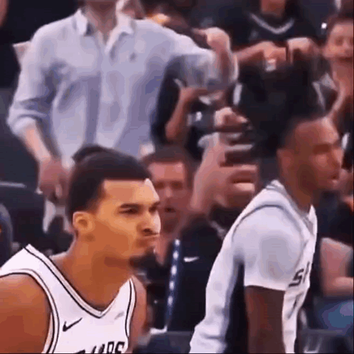 Two Basketball Players Are Sitting In The Stands During A Game And One Of Them Is Making A Funny Face . GIF