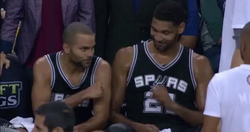 Two Basketball Players Are Sitting In The Stands Talking To Each Other During A Game . GIF