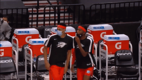 Two Basketball Players Wearing Face Masks Are Standing In Front Of A Row Of Gatorade Coolers GIF