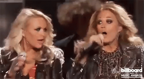 Two Blonde Women Are Standing Next To Each Other On A Stage Holding Microphones . GIF