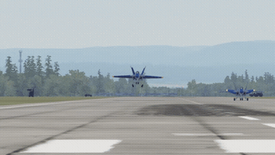 Two Blue Jets Are Taking Off From A Runway With Trees In The Background GIF