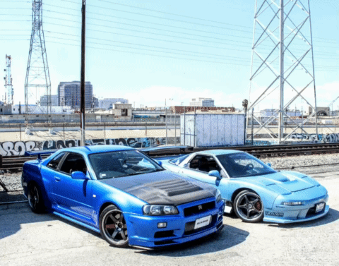 Two Blue Sports Cars Are Parked Next To Each Other With Graffiti On The Wall Behind Them That Says ' Pop ' GIF