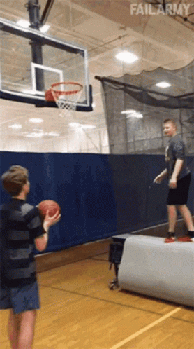 Two Boys Are Playing Basketball In A Gym With Failarmy In The Corner GIF