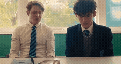 Two Boys Are Sitting At A Desk In A Classroom . GIF