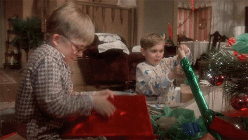 Two Boys In Pajamas Are Opening Christmas Presents In Front Of A Christmas Tree GIF