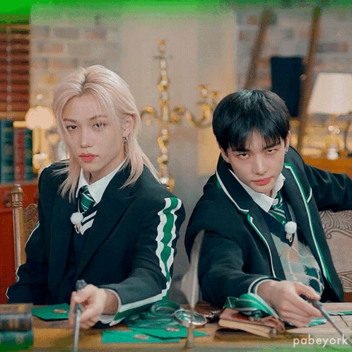 Two Boys In Suits And Ties Are Sitting At A Table With A Green Background That Says Pabeyork On It GIF