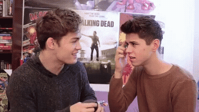 Two Boys Sitting In Front Of Walking Dead Poster GIF