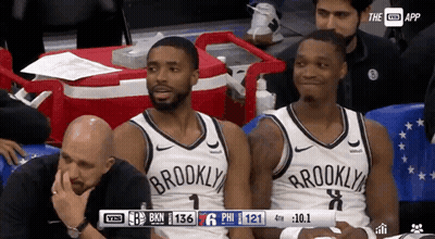 Two Brooklyn Nets Players Sit In The Stands During A Basketball Game GIF