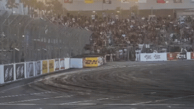 Two Cars Are Drifting On A Track With A Crowd In The Background And A Sign That Says Jcte GIF
