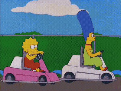 Two Cartoon Characters , Lisa Simpson And Marge Simpson , Are Driving Go Karts On A Track . GIF