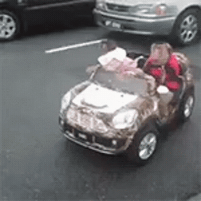 Two Children Are Riding In A Toy Car On The Street GIF