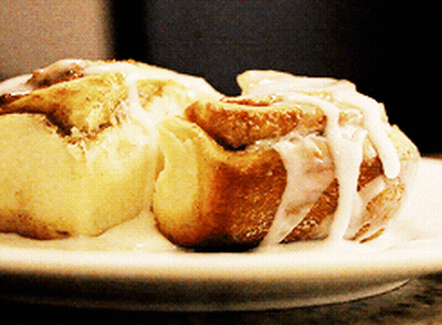 Two Cinnamon Rolls On A White Plate With Icing On Them GIF