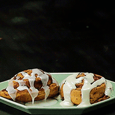 Two Cinnamon Rolls With White Frosting On A Plate GIF