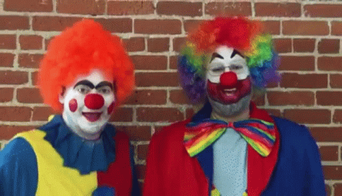 Two Clowns Are Standing Next To Each Other In Front Of A Brick Wall And Smiling . GIF
