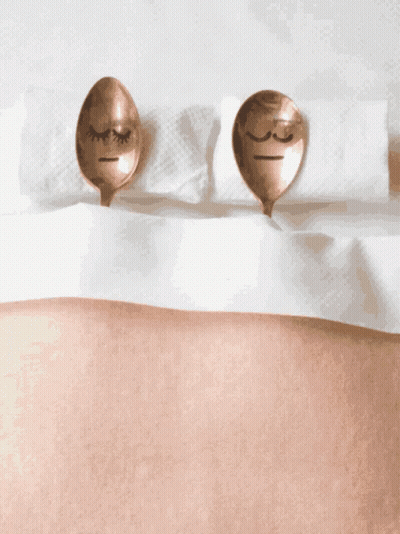 Two Copper Spoons With Faces Drawn On Them Are Laying On A Bed GIF