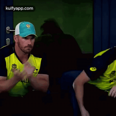 Two Cricket Players Are Sitting Next To Each Other In A Dark Room . GIF