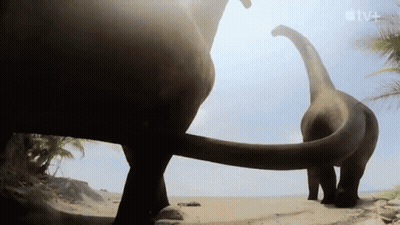 Two Dinosaurs Standing On Beach With TV+ Logo GIF