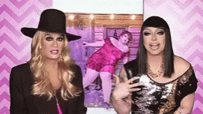 Two Drag Queens Are Standing Next To Each Other In Front Of A Picture Of A Fat Woman . GIF