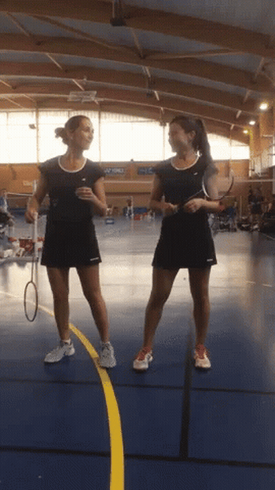 Two Female Badminton Players Standing Next To Each Other On A Blue Court GIF