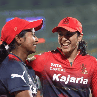 Two Female Cricket Players Are Standing Next To Each Other On The Field And Smiling . GIF