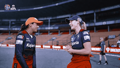 Two Female Cricket Players Wearing Kalari Jerseys Laugh Together GIF